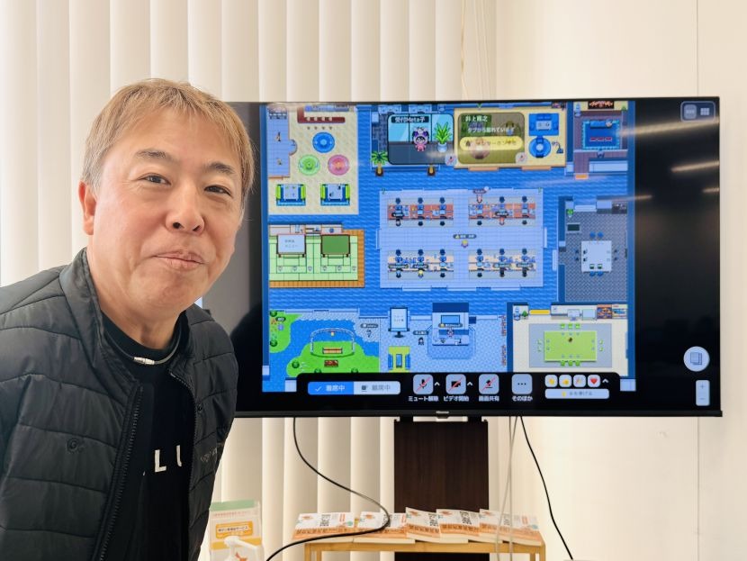 『MetaLife』を表示するモニターの前に立つ賀村さん